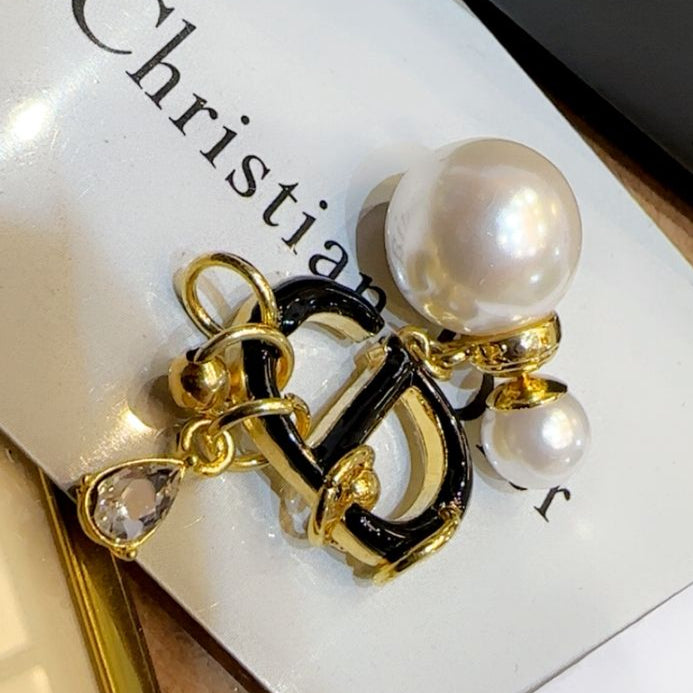 Gold and black earrings with pearls on a white surface with 'Christian' branding.