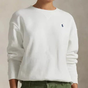 Person wearing a white sweatshirt with a logo and green pants against a beige background